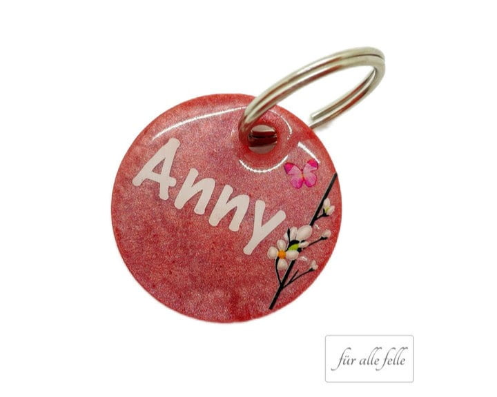Personalisierte runde Hundemarke in Rot mit dem Namen 'Anny', verziert mit zarten Blumen und einem schimmernden Finish, handgefertigt von 'Für alle Felle'.