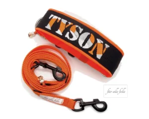 Breites Hundehalsband in Schwarz mit dem Namen 'Tyson' in einem Camouflage-Stil in Weiß und Orange, zusammen mit einer passenden orangefarbenen Leine von 'Für alle Felle'